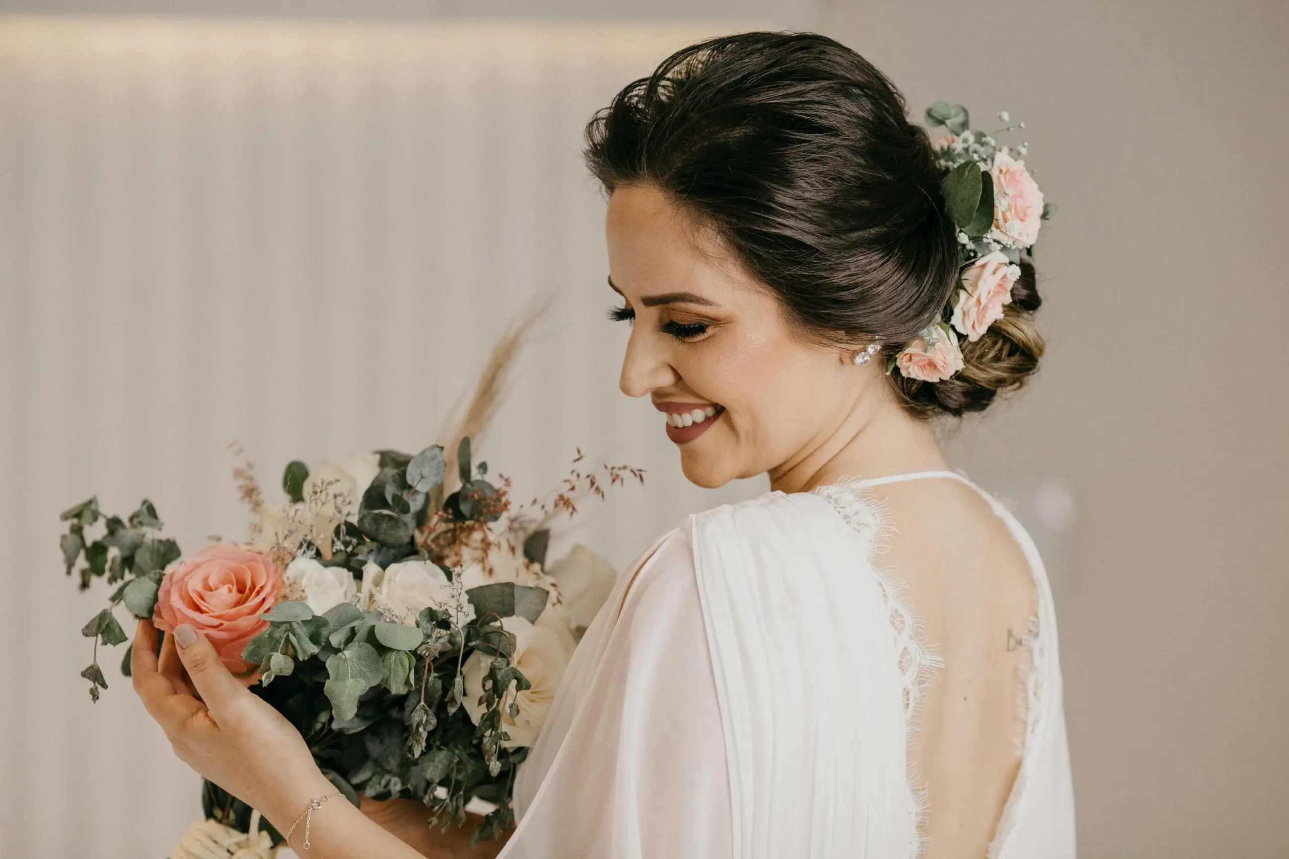 Smiling bride with elegant updo hairstyle and floral hair accessories holding her wedding bouquet in Ennis TX